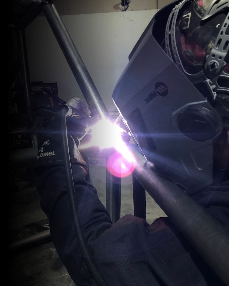 Weldability Welder using protective helmet welding steel tubing in a fabrication workshop, showing precision welding and material durability.