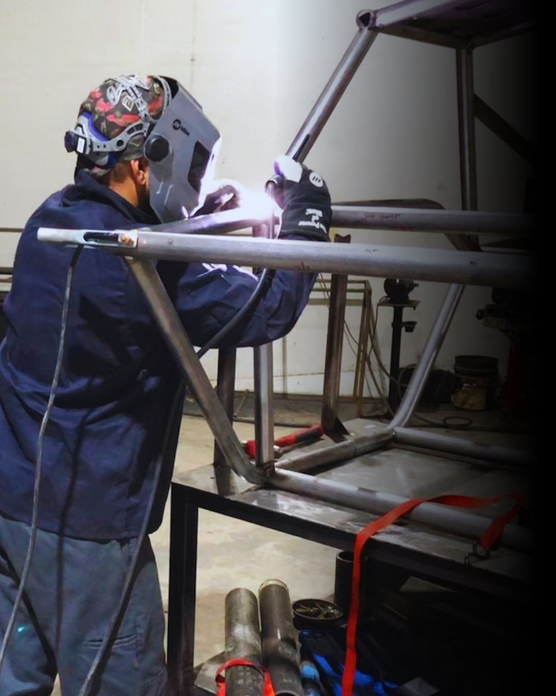 Workability Welder assembling a steel frame structure using welding equipment in a fabrication shop, highlighting precision and structural work.